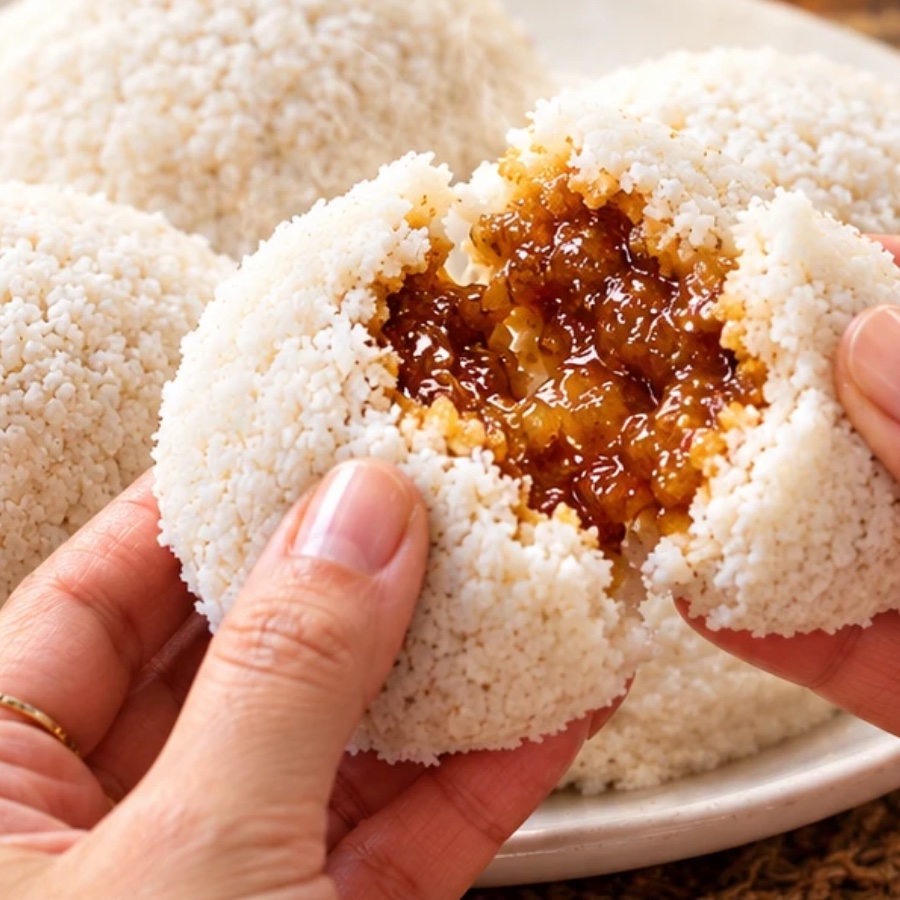 Vapa pitha broken open in two hands, showing the dark molten filling inside a soft steamed rice cake